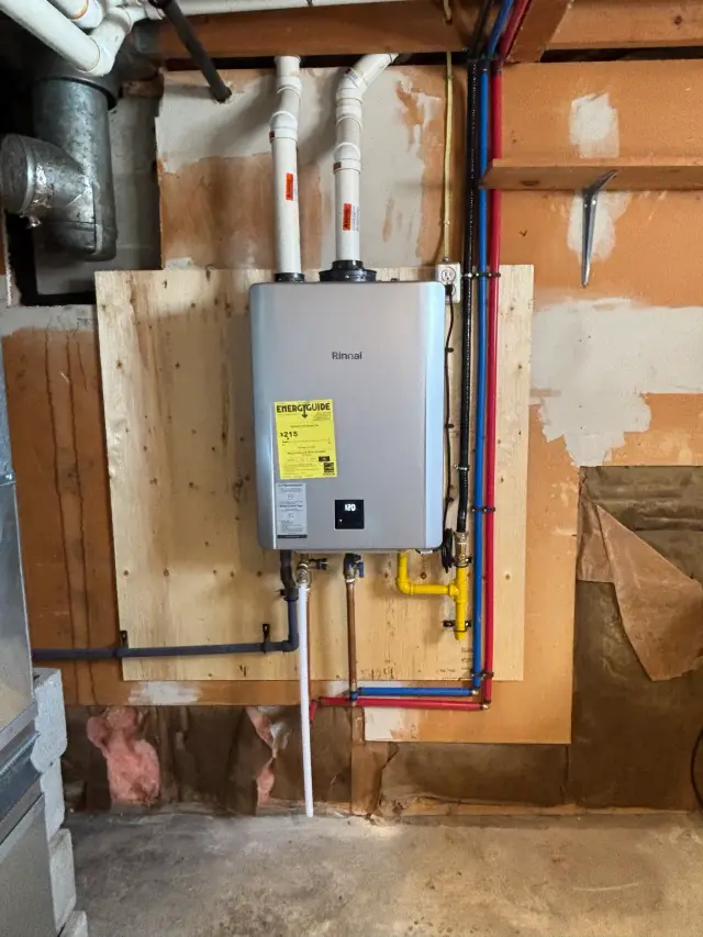 A Rinnai tankless water heater is mounted on a wooden board against a partially finished wall with exposed