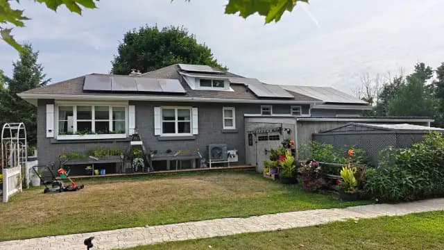 Solar panels on the roof of a house with a lawn and garden in the foreground