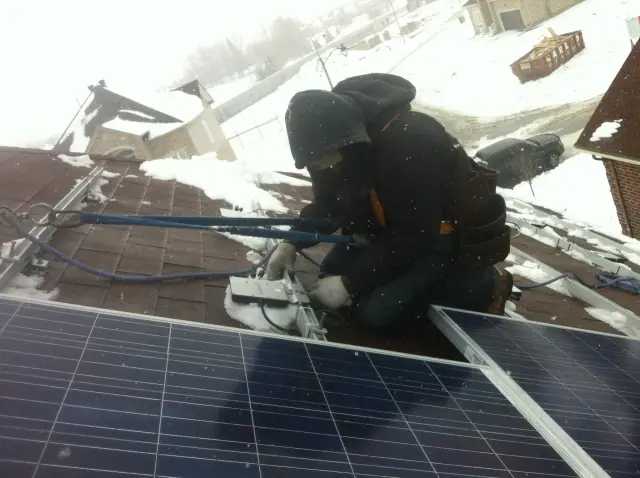 A is installing solar panels on a roof covered in snow, with houses and a car visible in