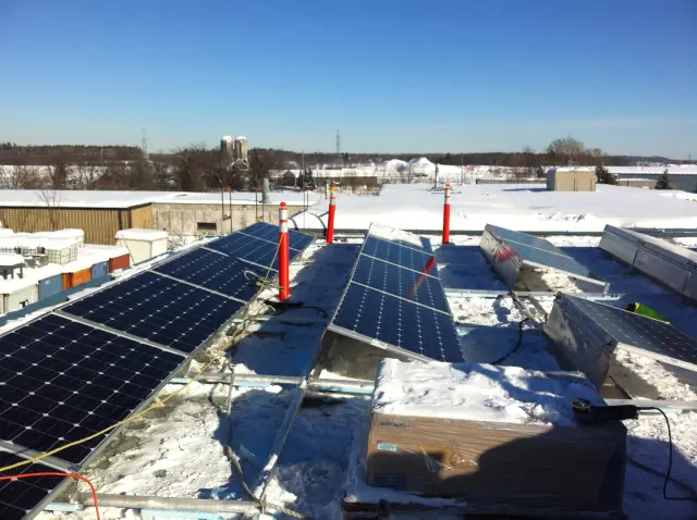 Solar panels on a rooftop covered in snow, with orange safety cones and cables visible