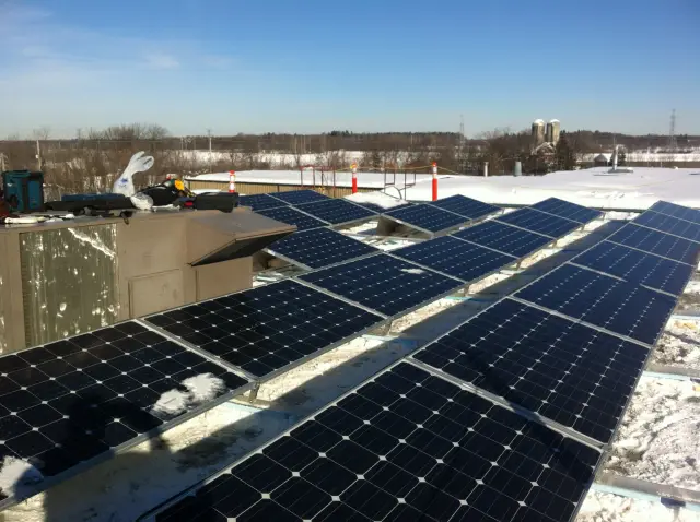Solar panels on a flat roof with snow around, with a clear blue sky in the background