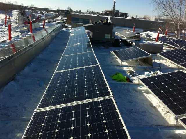 Solar panels on a rooftop covered in snow with orange safety cones around