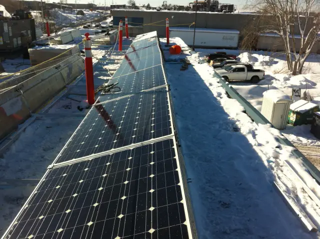 Solar panels on a roof with snow around them, showing the clear sky above